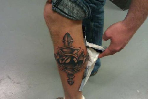 Man Showing His Cross Tattoo On Left Leg
