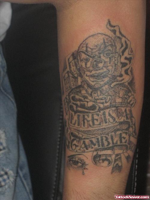 Grey Ink Joker Head and Life Is A Gamble Banner Tattoo On Arm