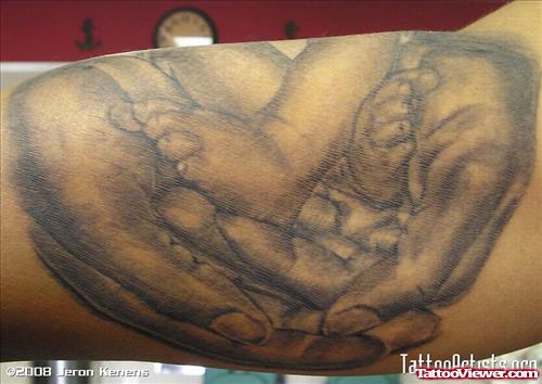 Grey Ink Baby Feet In Hands Tattoo On Bicep