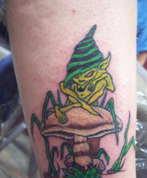 Green Ink Goblin Sitting On Mushroom Tattoo