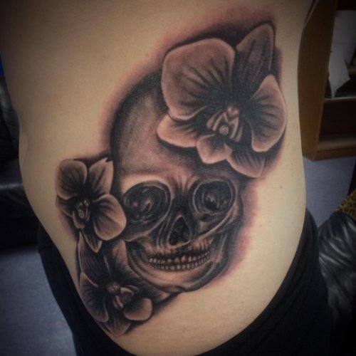 Grey Ink Skull And Orchid Tattoos On Side Rib